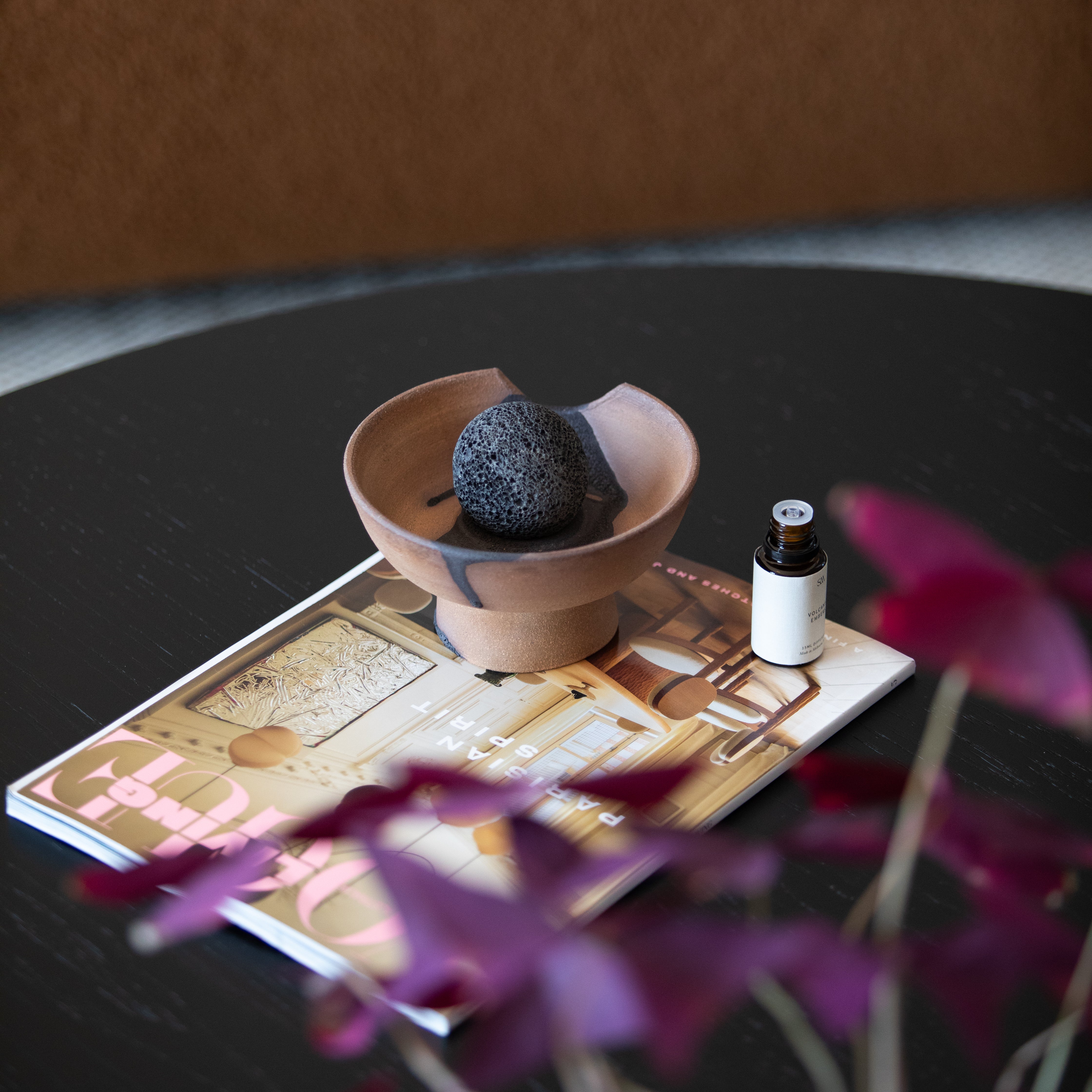 Red Santal fragrance oil in amber glass bottle beside ceramic tray and volcanic rock