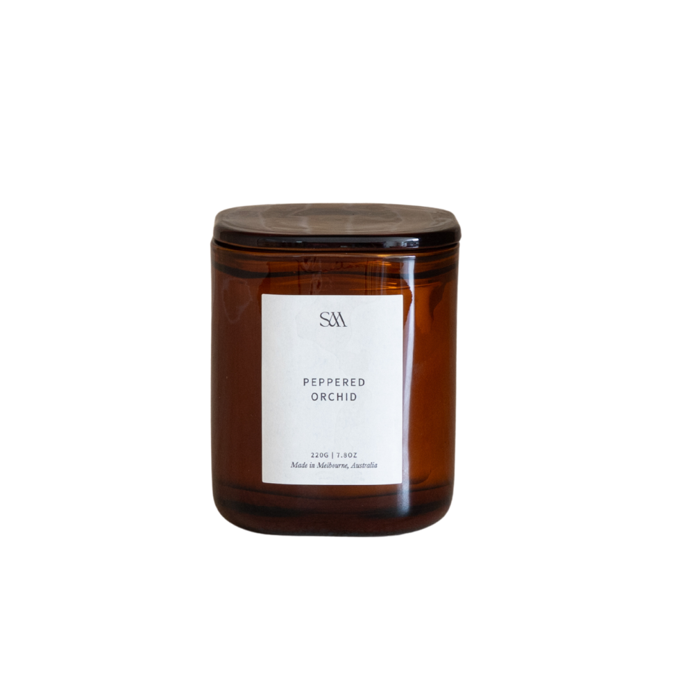 An amber glass jar candle with a dark brown lid and a white label reading 'SW' and 'PEPPERED ORCHID' on a plain white background.