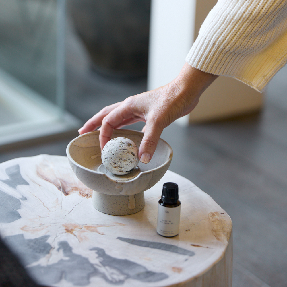 Hand placing pumice stone in Lunara Diffuser by Studio McKenna — styled with Coastal Wilderness oil on natural timber
