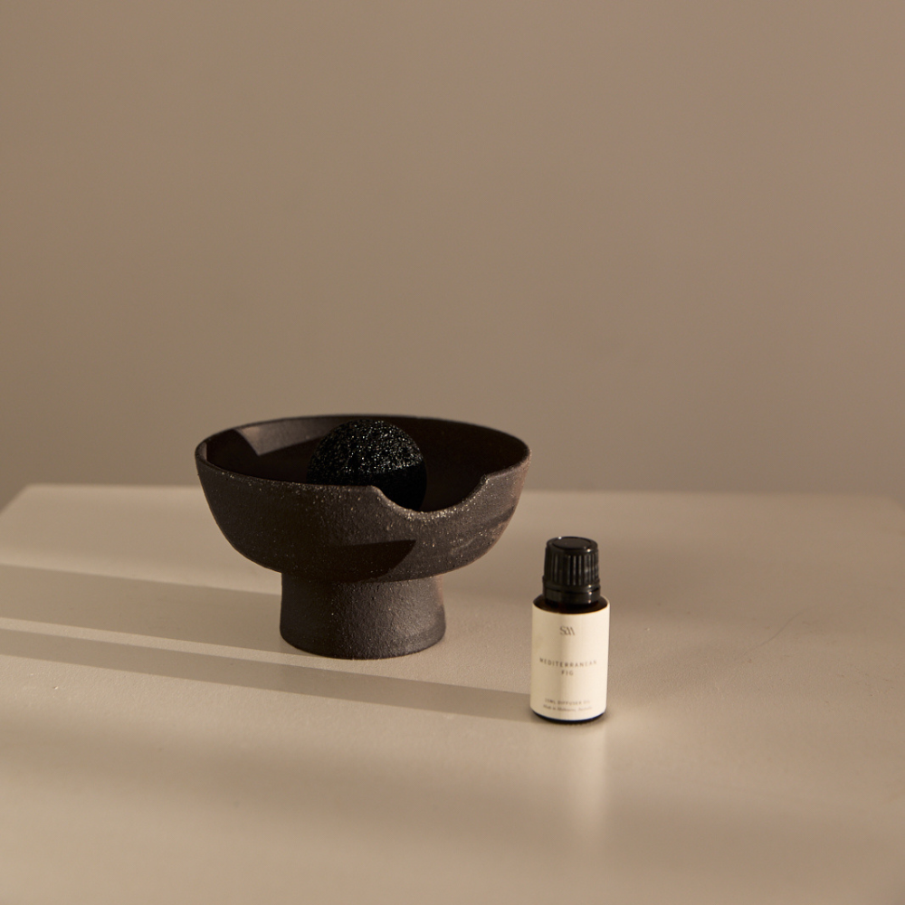 Peppered Orchid fragrance oil in amber glass bottle beside ceramic tray and volcanic rock