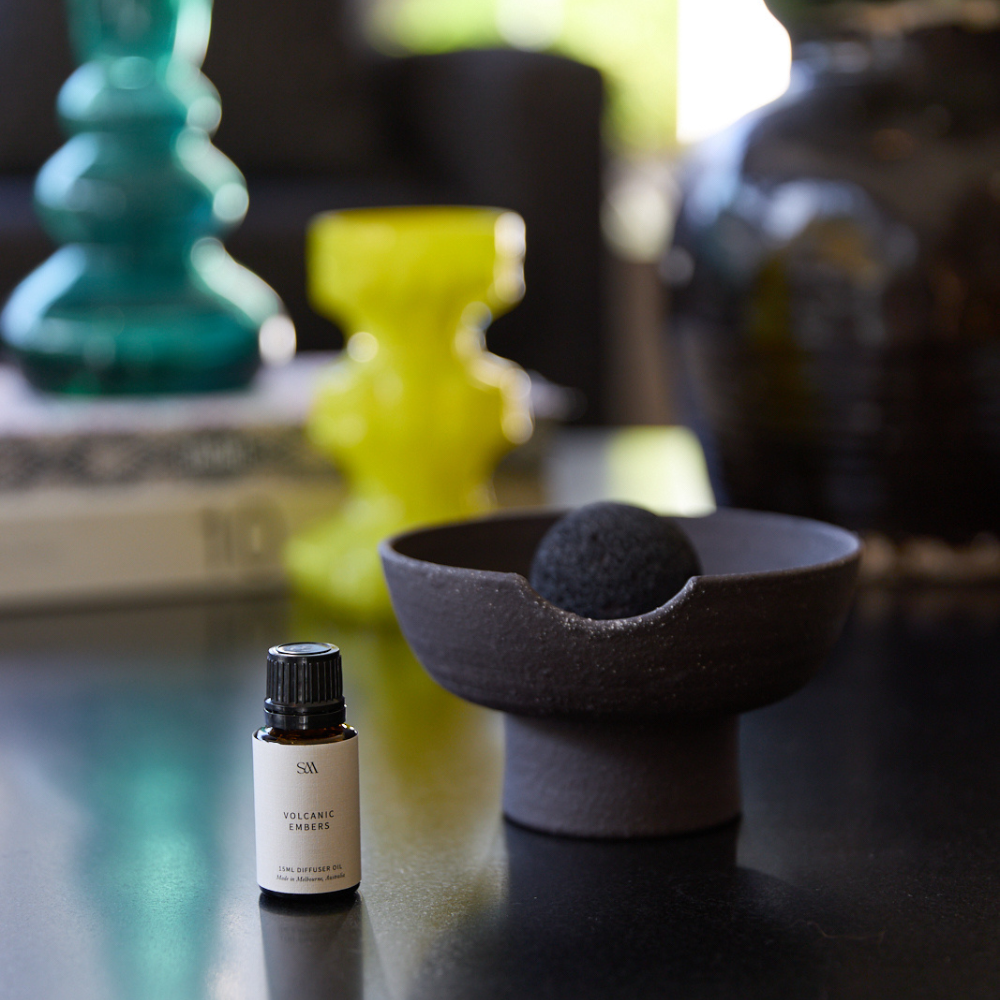 Volcanic Embers fragrance oil in amber glass bottle beside ceramic tray and volcanic rock