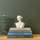 Bust white candle of Artemis Diana sitting on a stack of books styled with two green vases